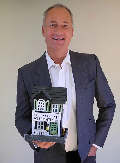 Werner Jüngling der Inhaber des Immobilienunternehmens Werner Jüngling in Göppingen hält ein dekoratives Modellhaus mit dem Schriftzug ‚Willkommen‘.